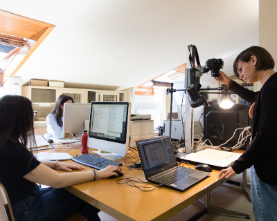 Three women working together at a computer in an office, demonstrating teamwork and concentration on their tasks.