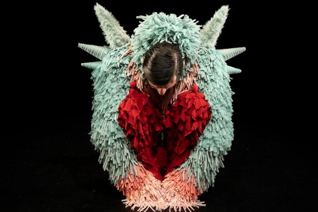 A bowed human figure, wrapped in wings