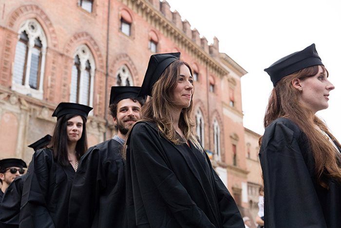 Due ragazze con il tocco che guardano dentro a una pergamena come fosse un binocolo.