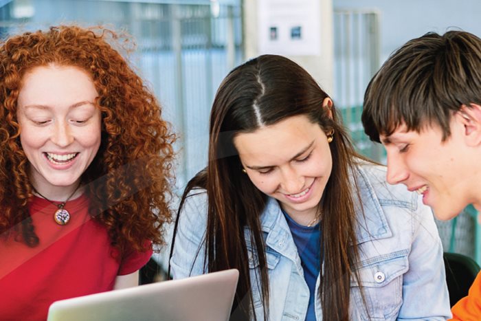 Gruppo di studentesse e studenti sorridenti che lavorano insieme al computer portatile in uno spazio interno.