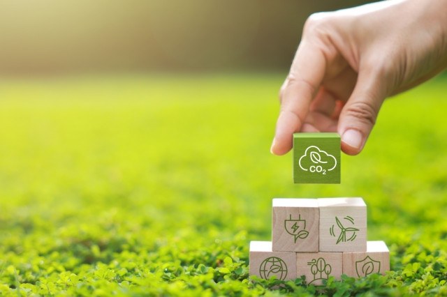 Mano che posiziona un cubo verde con un’icona di una foglia e la scritta “CO₂” sopra altri cubi di legno che mostrano simboli legati all’energia rinnovabile